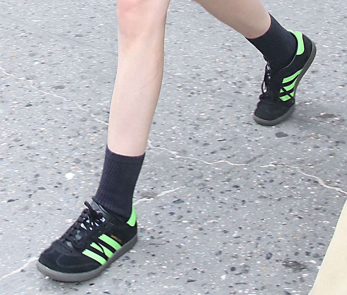 Kristen Stewart gives tailoring a sporty twist with her Adidas “Samba Deco SPZL” sneakers in Core Black with Lucid Lime Green stripes, featuring decorative stitching and zigzag panels around the eyelets