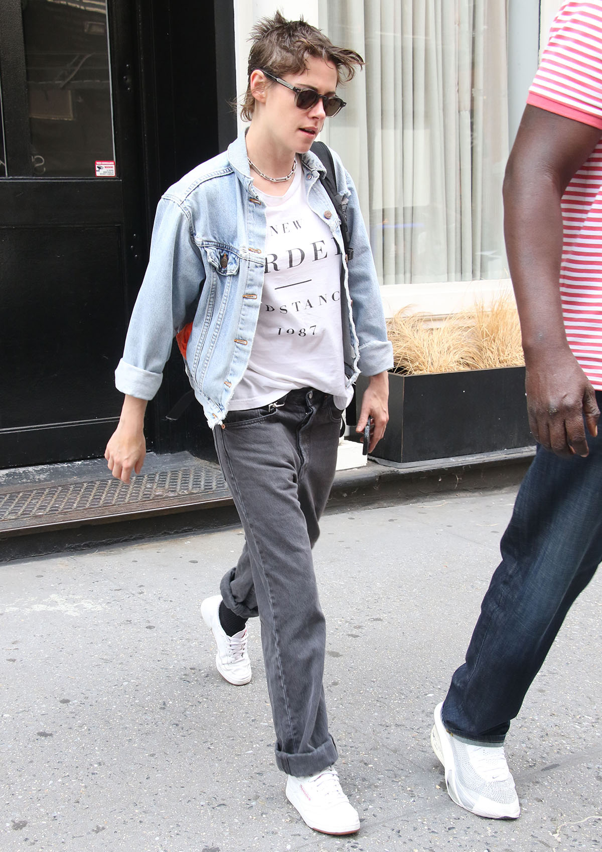 Kristen Stewart channels relaxed ’90s street style in New York, pairing Reebok Club C 85 sneakers with loose charcoal denim, a New Order tee, and an oversized denim jacket