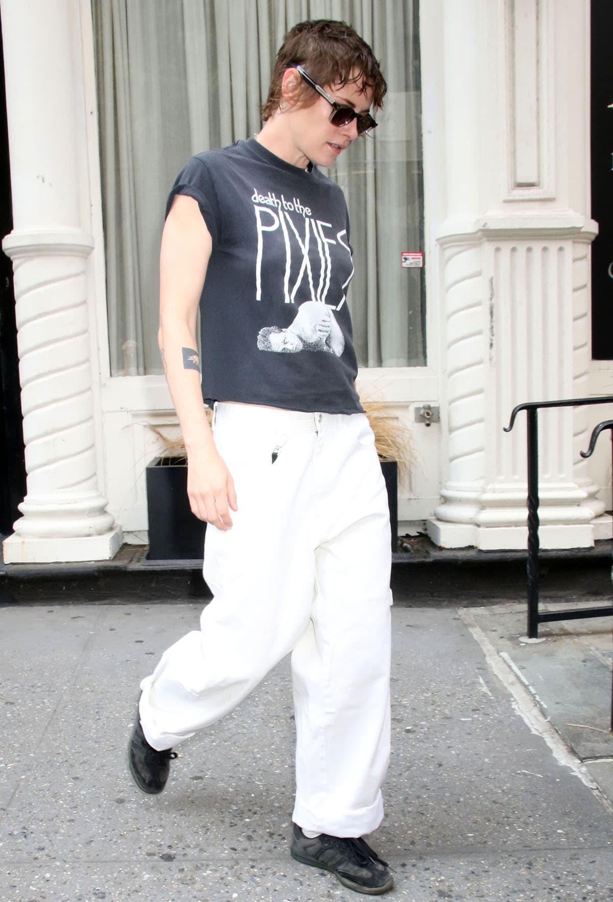 Kristen Stewart teams her black Adidas Samba sneakers with white jeans and a faded black vintage-style band tee featuring artwork from alternative rock band The Pixies