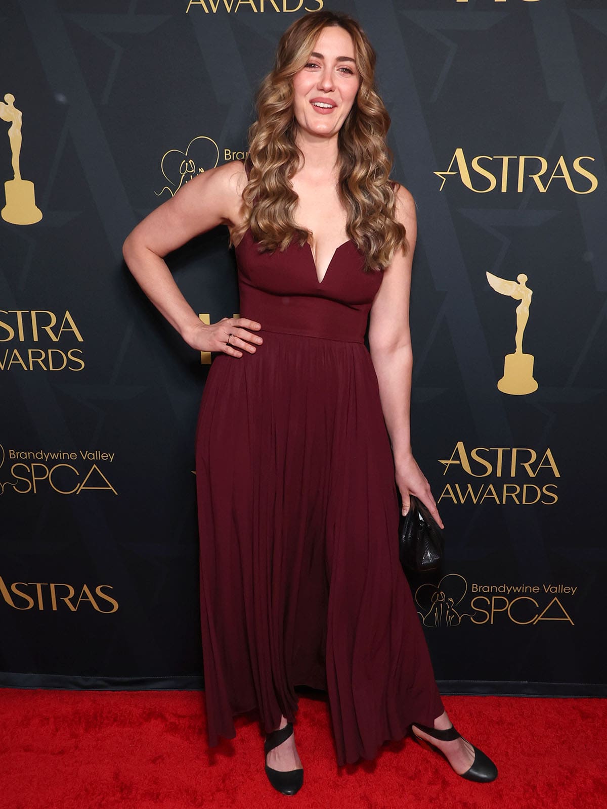 Madeline Zima goes for a romantic look, wearing the deep burgundy La Ligne “Carey” crepe dress featuring a V-neckline, shoulder straps, and a softly pleated, flowy skirt