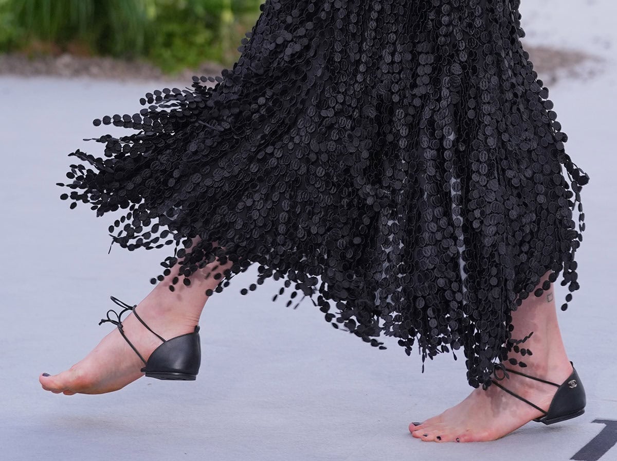 Margaret Qualley dares to wear Chanel's barely there heel cap shoes featuring just a heel cap with Chanel's double CC logo and two slim straps tied over the top of her feet