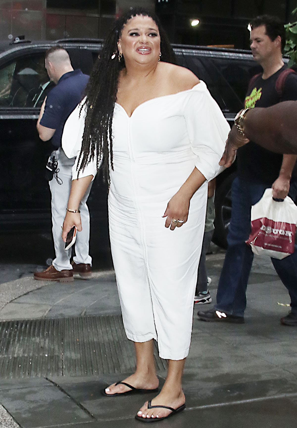 Michelle Buteau pairs her comfy flip-flops with a white Mara Hoffman dress featuring a structured off-the-shoulder silhouette, vertical stitching down the center, and a center front slit