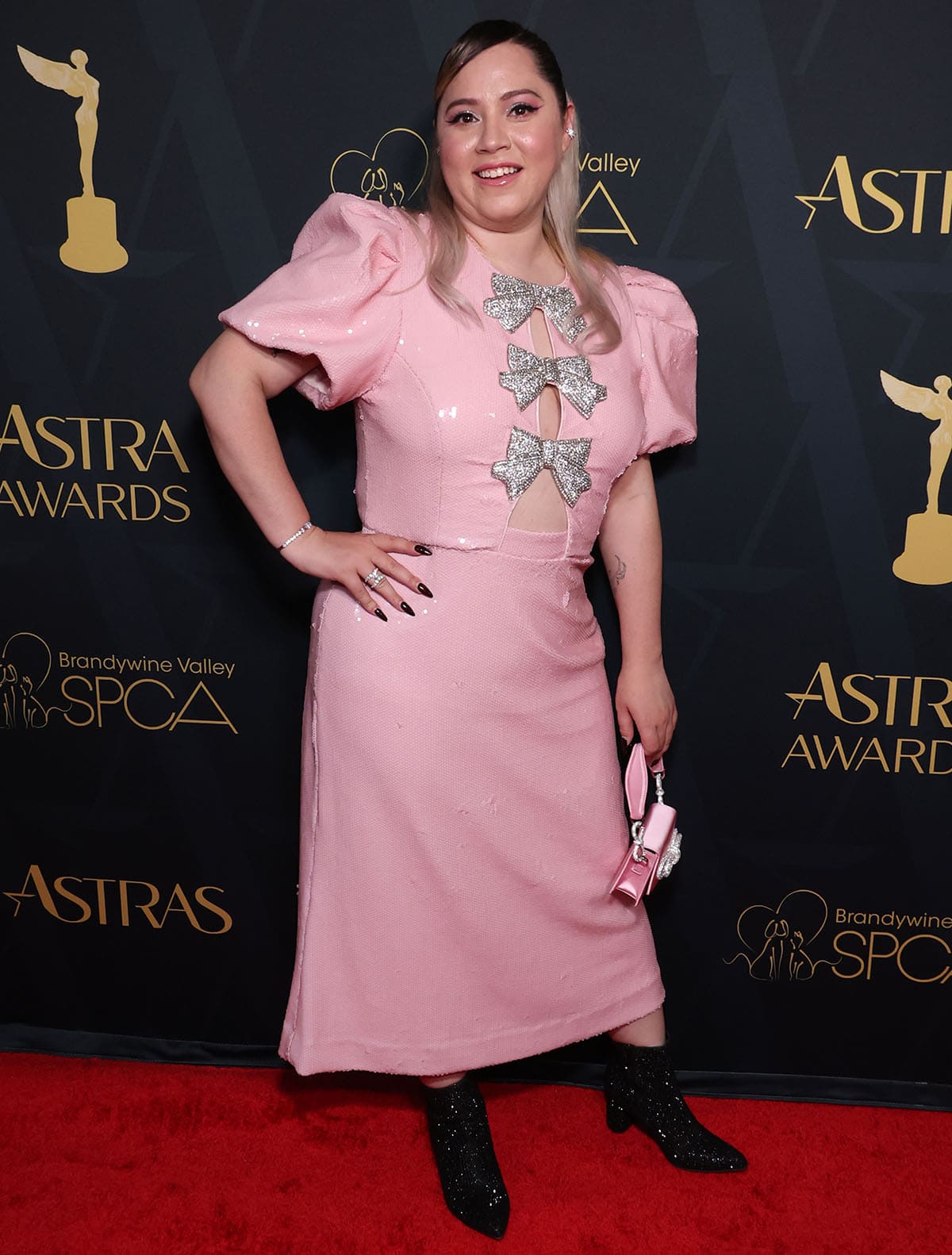 Vivienne Medrano pairs her black boots with a pink sequin-embellished Rebecca Vallance dress featuring voluminous puff sleeves, a midriff cutout, and crystal-encrusted bows