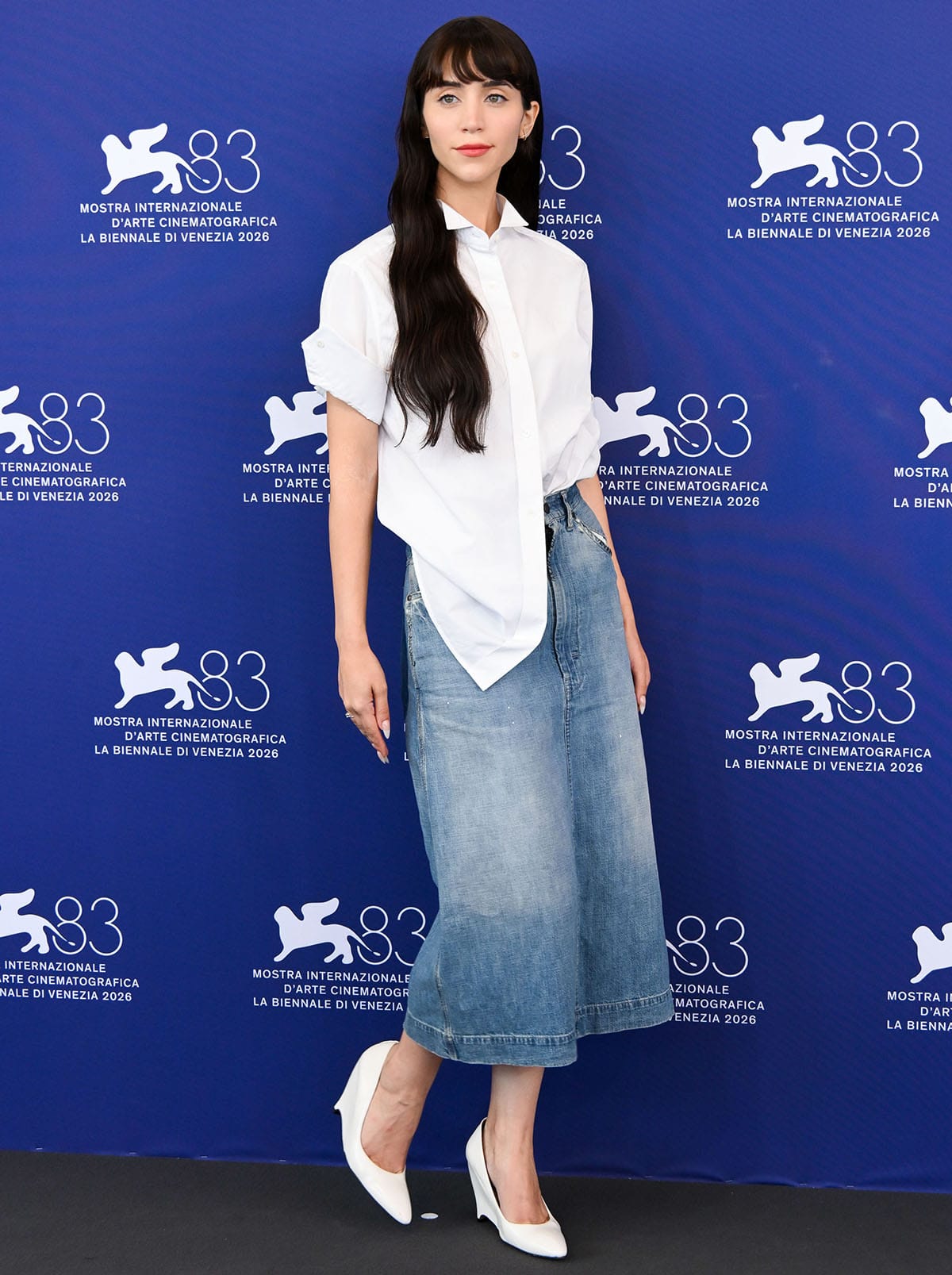 Caylee Cowan embraces relaxed summer tailoring in an oversized white shirt, French-tucked into a Maison Margiela denim midi skirt and paired with sculptural white wedge pumps