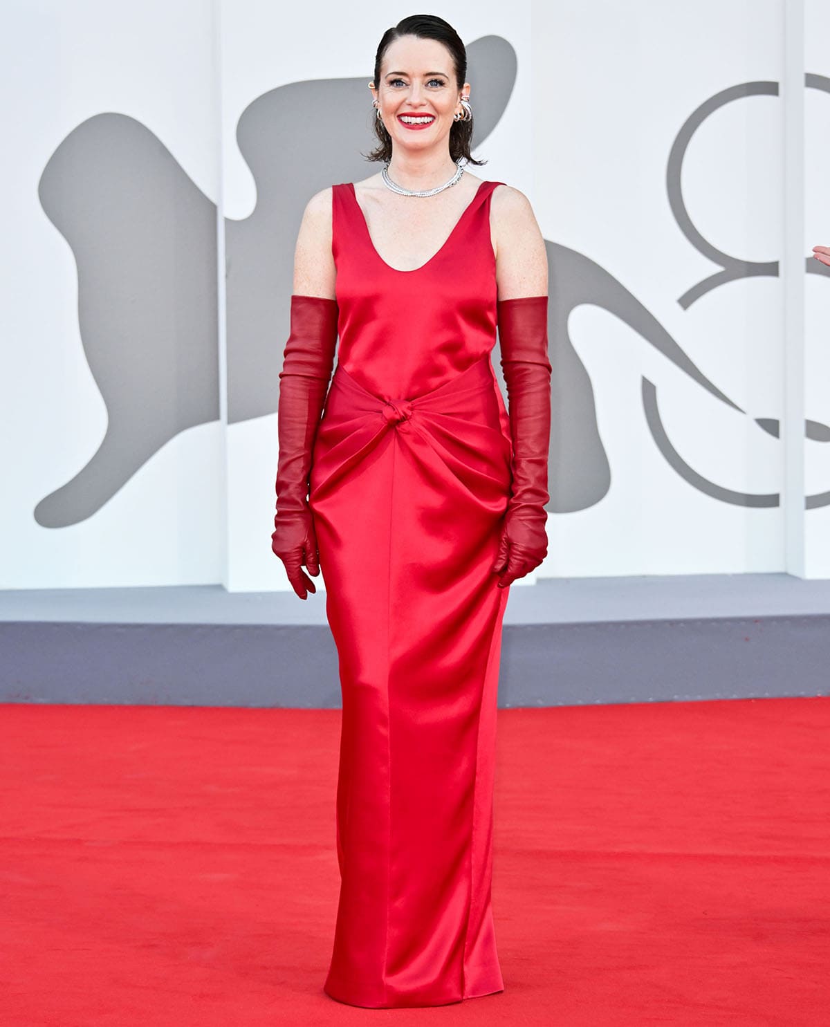 Claire Foy teams her red sandals with a Bottega Veneta red satin gown featuring a gathered knot detail at the waist and a pair of red leather opera gloves