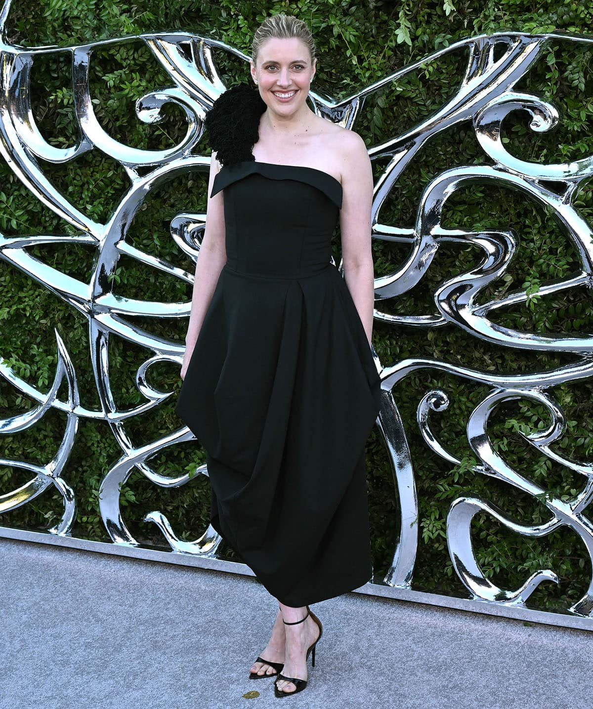 Greta Gerwig wears a black one-shoulder Ashlyn dress with Giuseppe Zanotti Intriigo sandals
