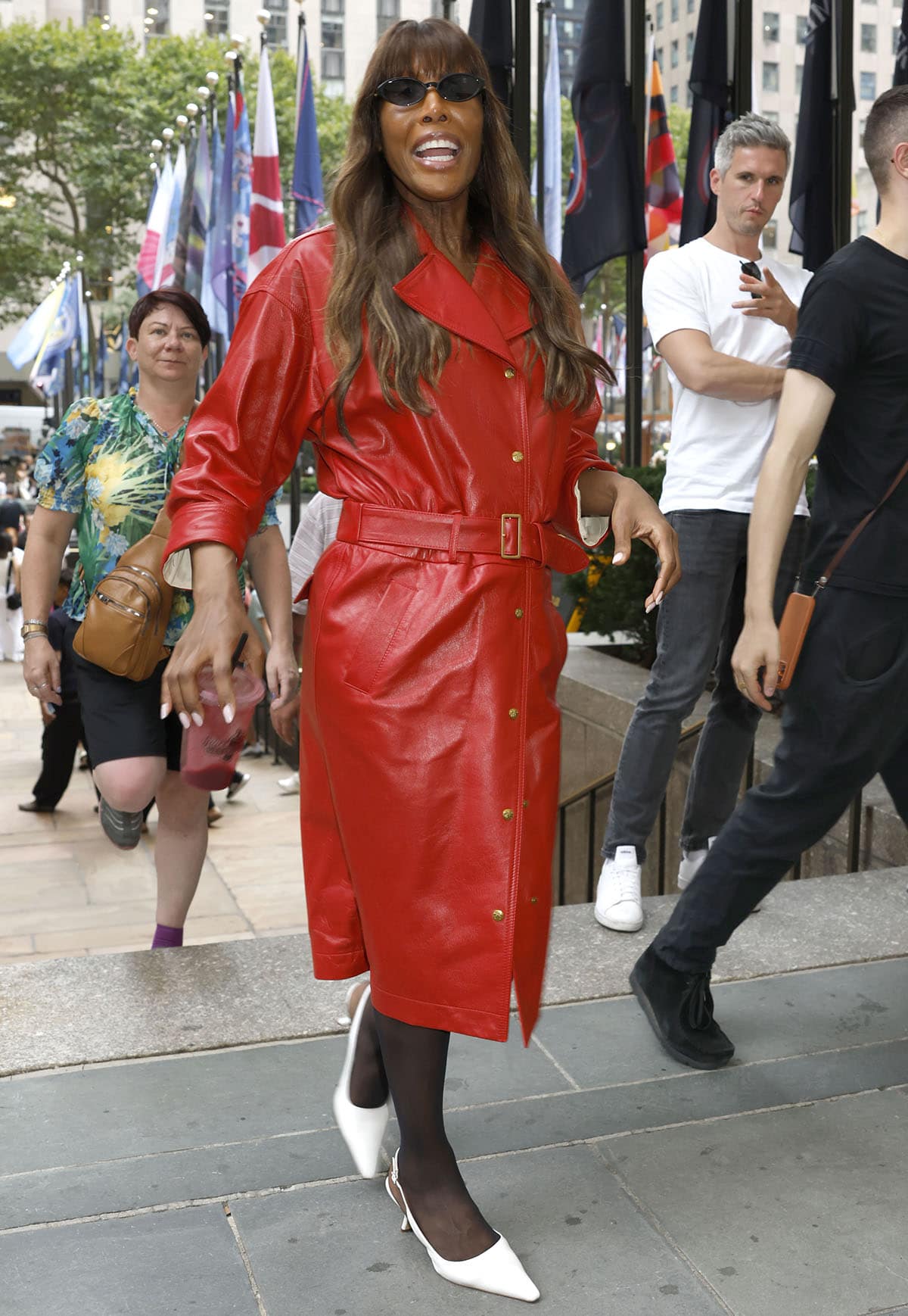 Iman makes a bold entrance in a cherry-red leather trench coat, sheer black stockings, and white Sam Edelman Bianka slingback pumps at the CFDA NYFW Live Ribbon Cutting Ceremony