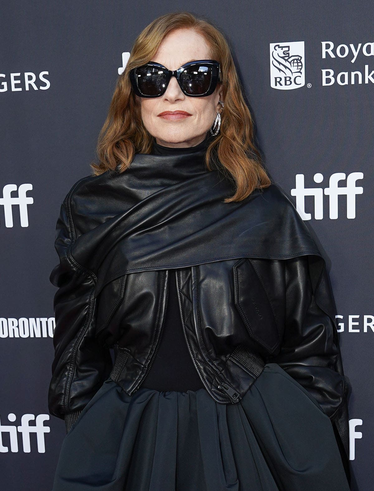 Isabelle Huppert wears oversized black cat-eye sunglasses, silver hoop earrings, and an architectural black Balenciaga leather jacket at TIFF 2026