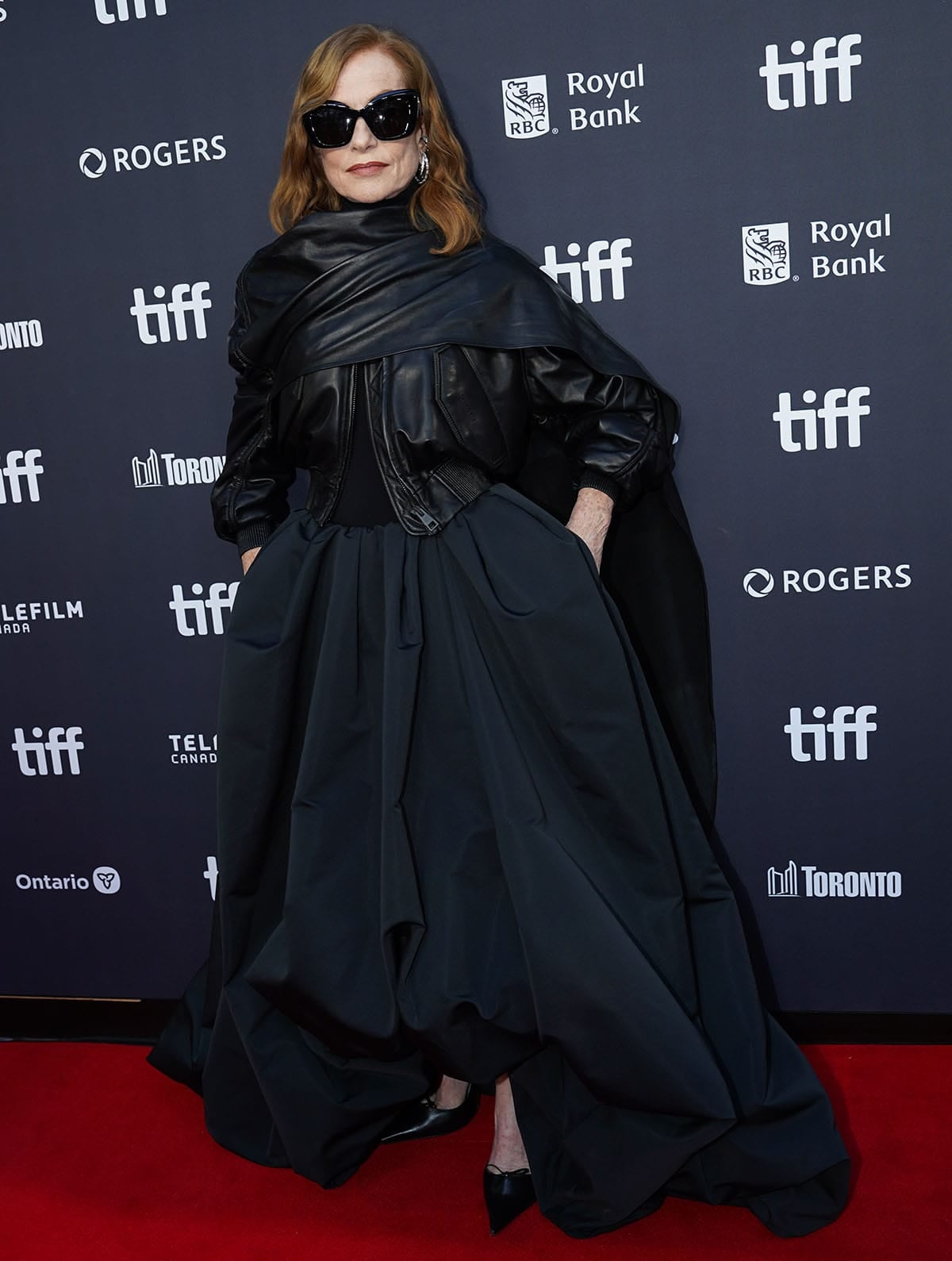 Isabelle Huppert wears a black Balenciaga leather bomber jacket, voluminous high-low ball skirt, and pointed sculptural pumps at the All About Corinne TIFF premiere