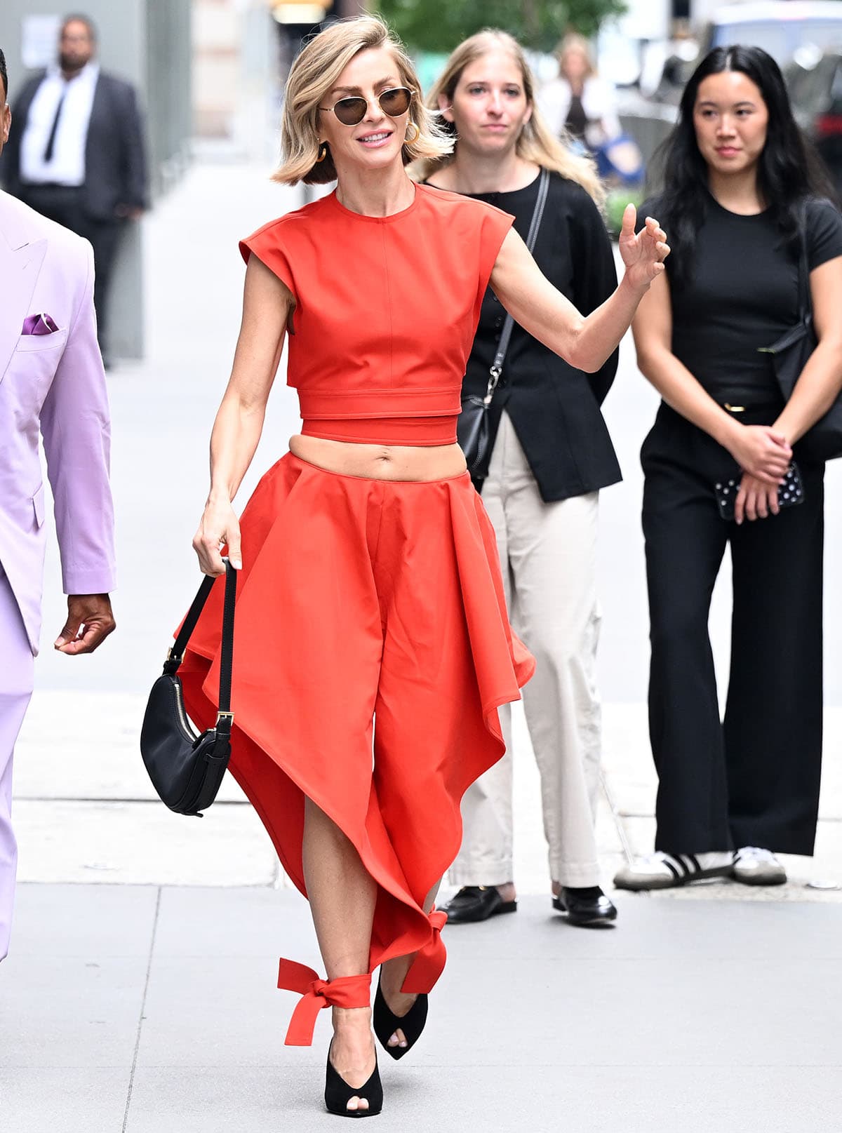 Julianne Hough pairs her black peep-toe mules with the blood-orange Alaia crop top and triangle pants set featuring asymmetrical tapered legs with side ruffles and thick ankle ties