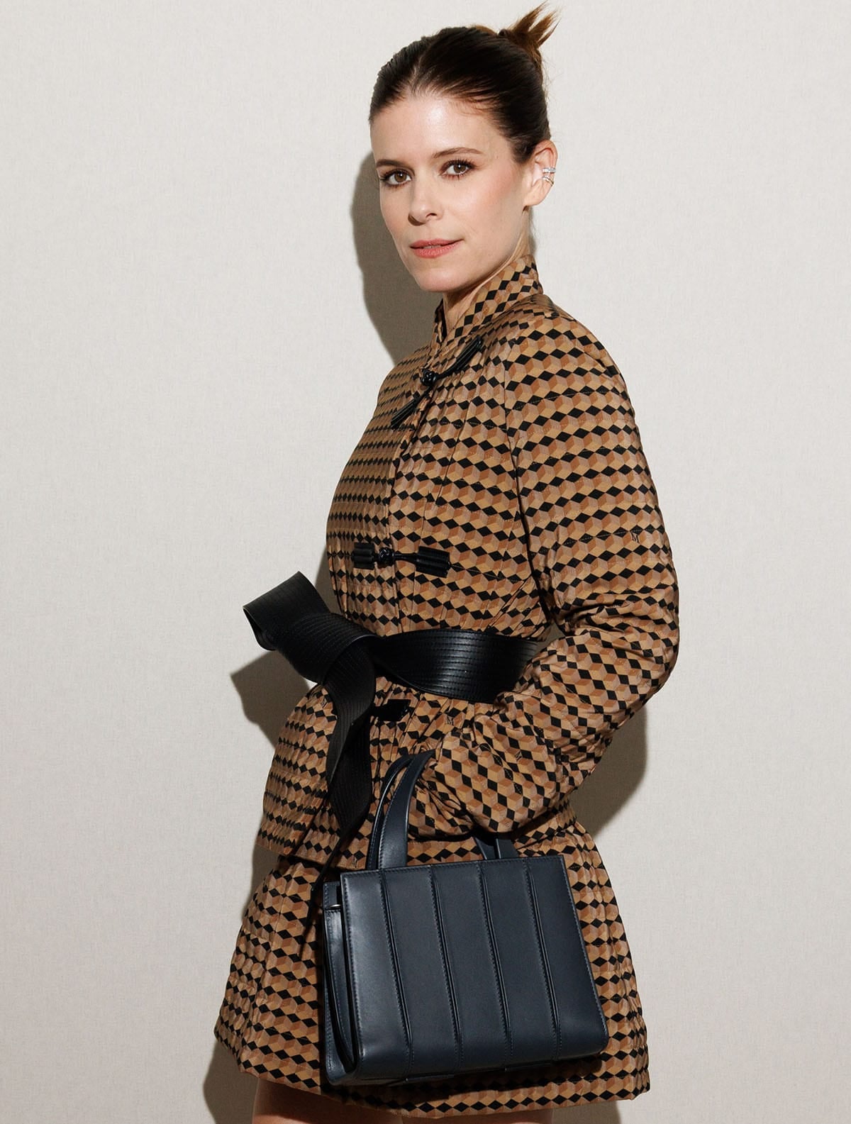 Kate Mara wears a sleek bun and ear cuffs while carrying a structured black Max Mara handbag