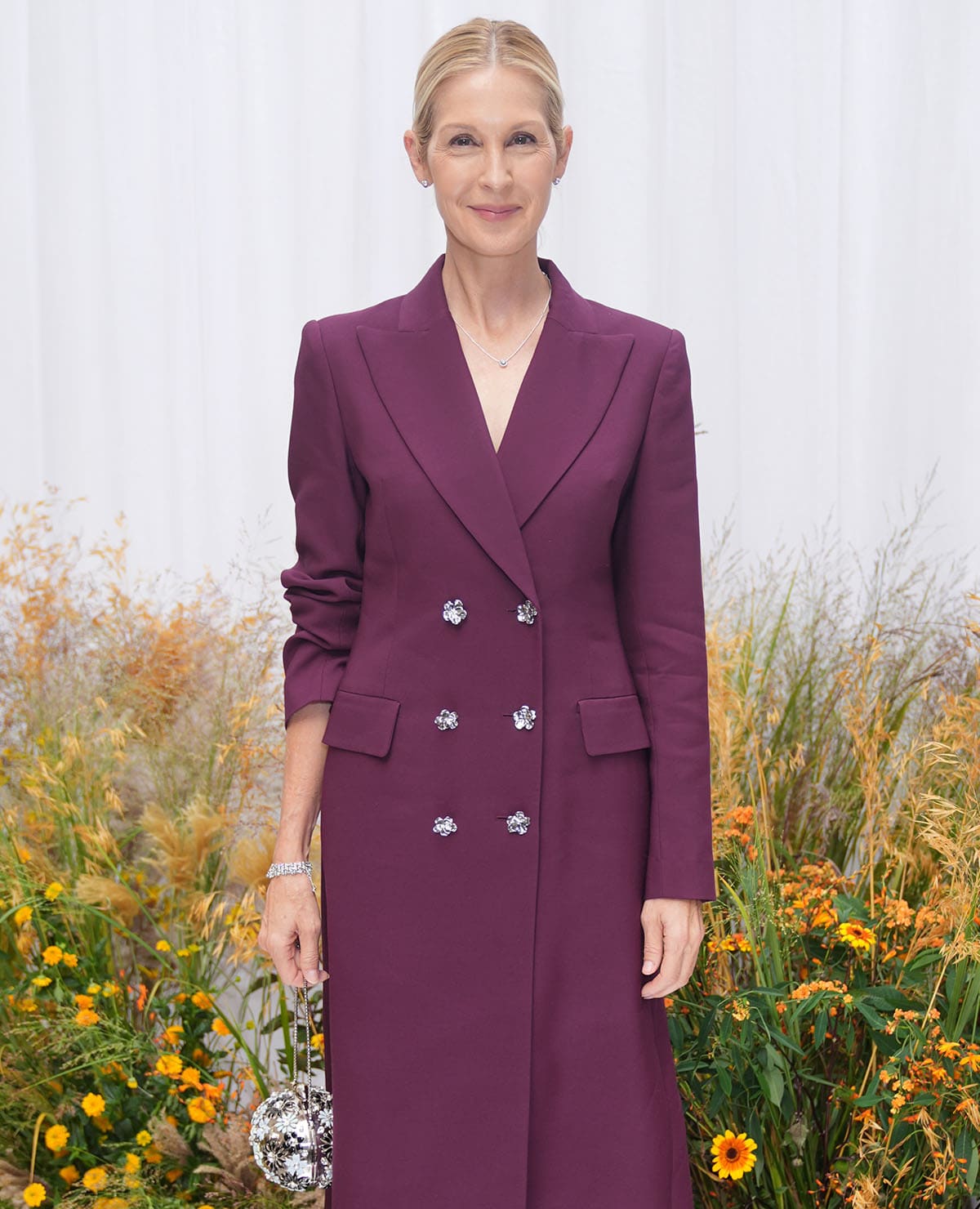 Kelly Rutherford carries a spherical silver floral evening bag with her plum Patrick McDowell coat dress at London Fashion Week