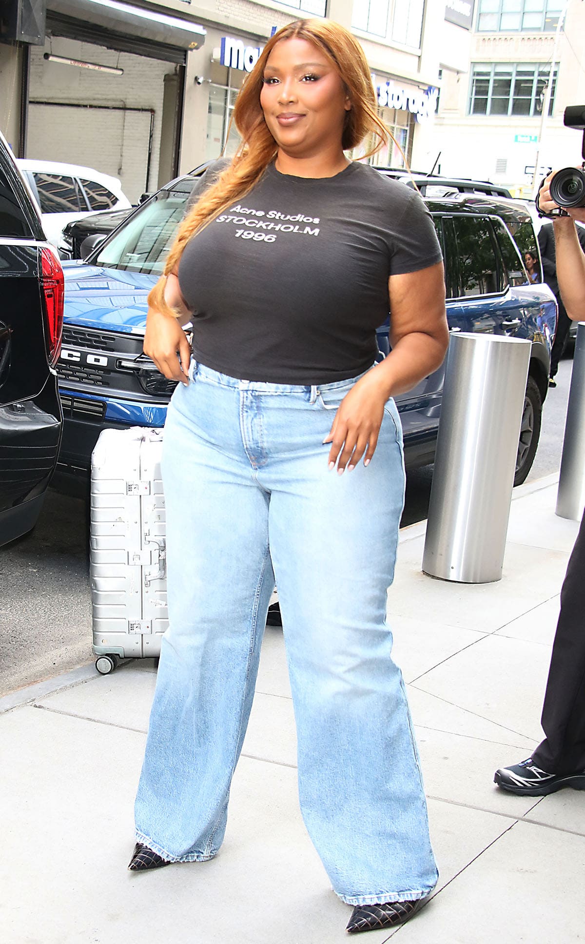 Lizzo elevates a black Acne Studios “Stockholm 1996” T-shirt and light-wash wide-leg jeans with glossy black croc-effect pointed-toe pumps