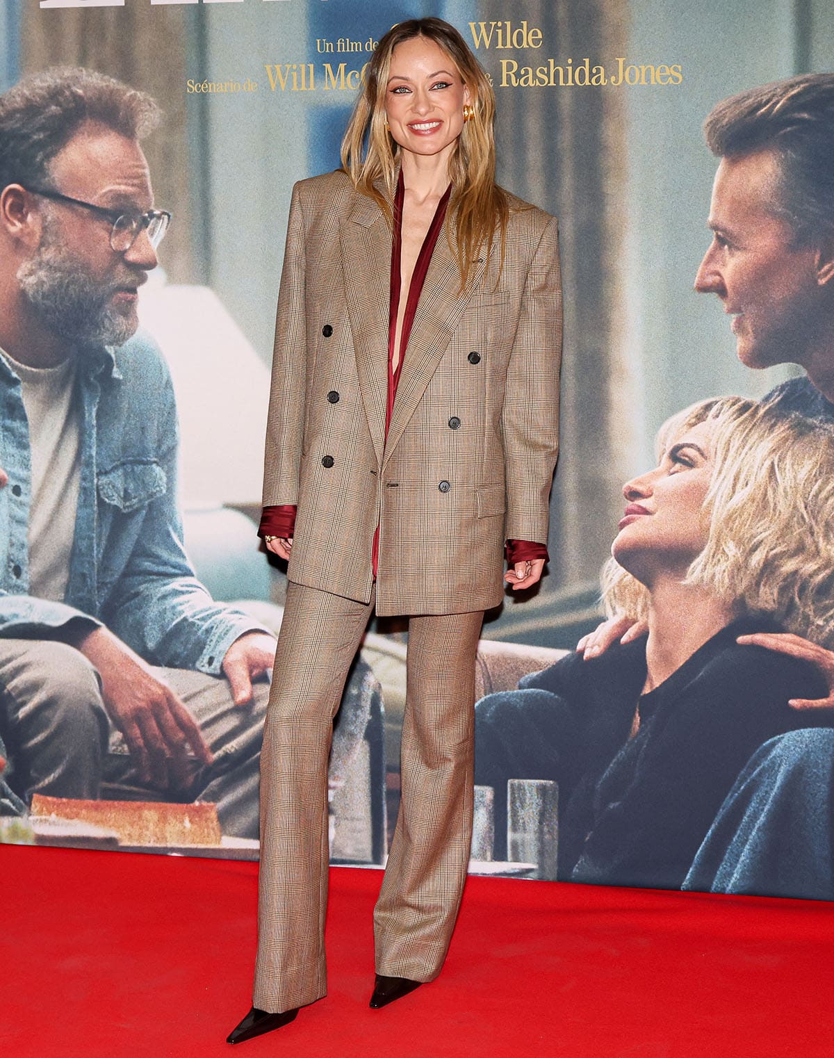 Olivia Wilde in an oversized brown checked Saint Laurent blazer and matching flared trousers layered over a burgundy silk blouse