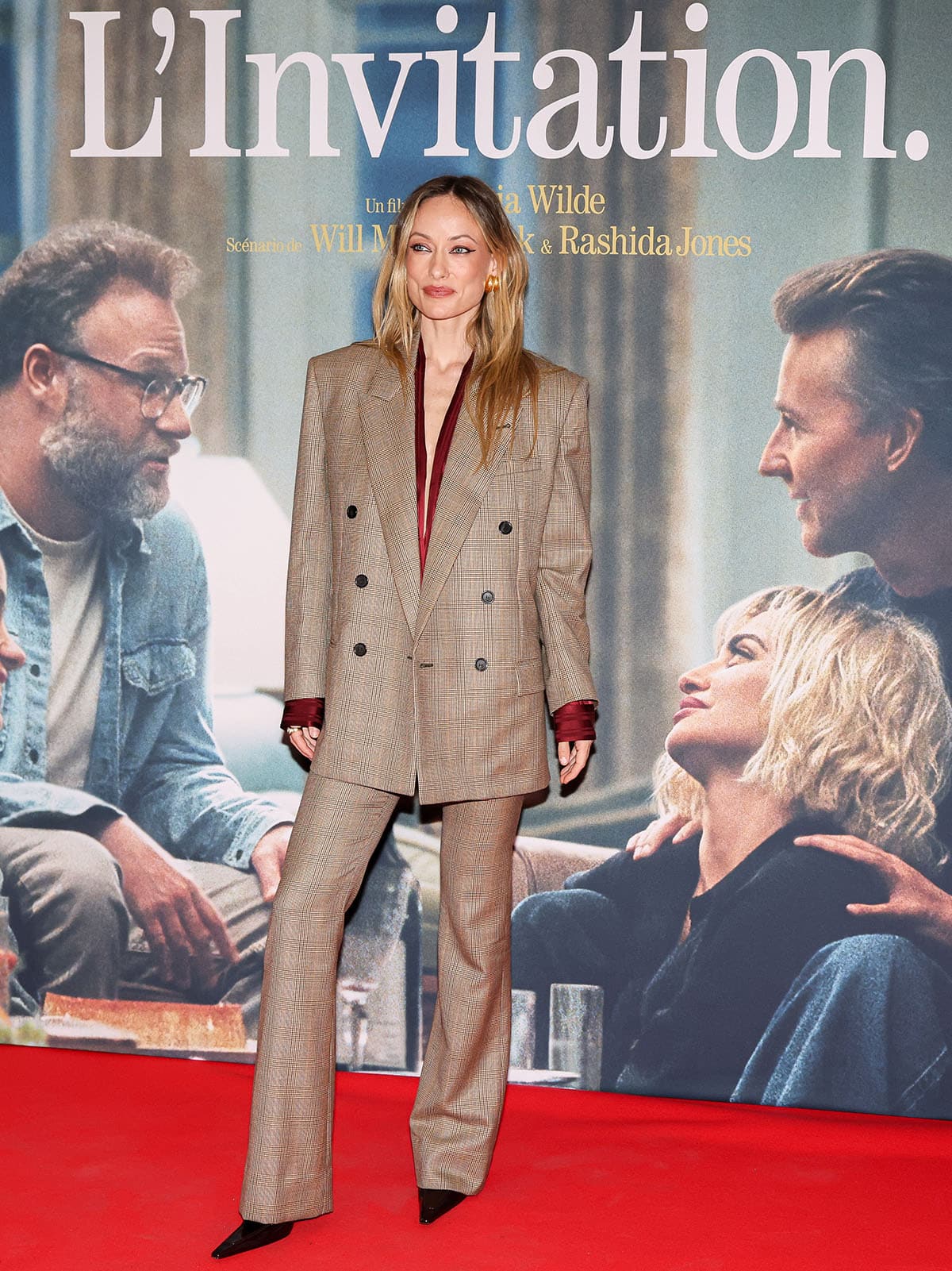 Olivia Wilde wearing a brown Prince of Wales checked Saint Laurent suit, burgundy silk blouse, and black pointed-toe pumps at The Invite Paris premiere