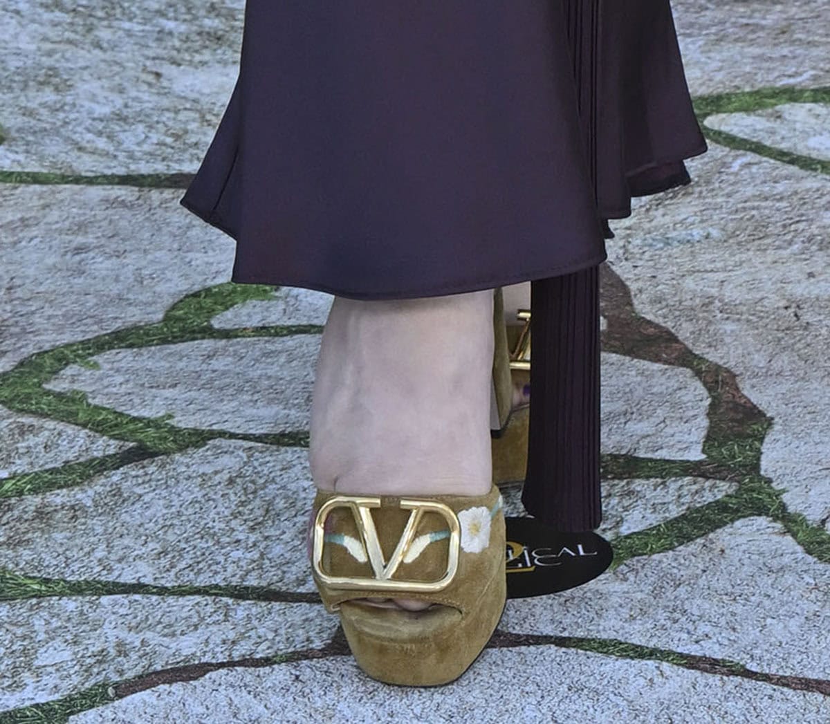 Stuart Brazell elevates her look with beige suede platform sandals by Valentino Garavani featuring floral embroideries and a gold-tone VLogo buckle at the front straps
